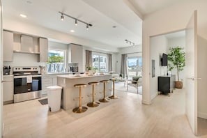 A modern kitchen with a central island, bar stools, and a dining area with a view.