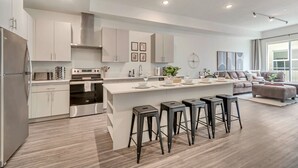 A modern kitchen with white cabinetry, a central island with stools, and a dining area with a sofa and coffee table. - Urban Retreat – Prime Location, Resort Amenities, Free Parking! (Salt Lake City)