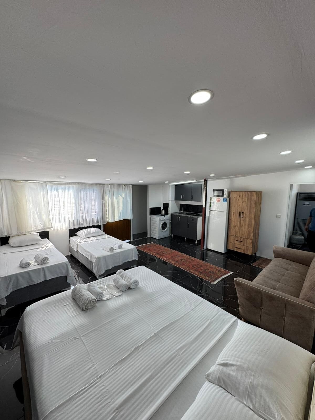 Hotellihuone, jossa on kolme sänkyä, pieni keittiö, kylpyhuone ja oleskelualue.