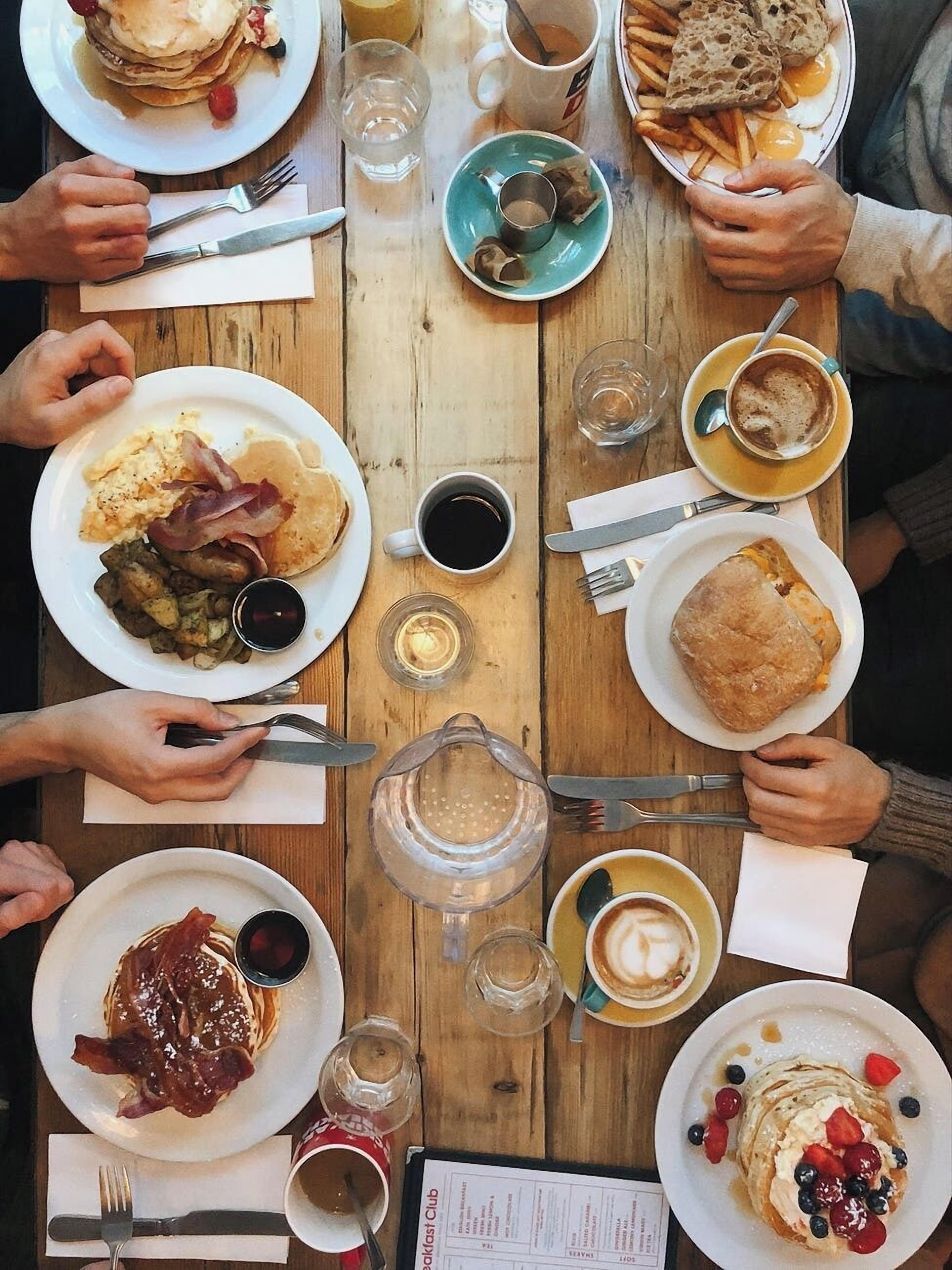 A wooden table with various breakfast items including pancakes, eggs, bacon, and toast.