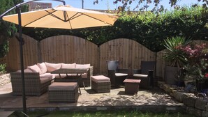 Une terrasse extérieure aménagée avec des meubles en osier, un grand parasol et une clôture en bois.