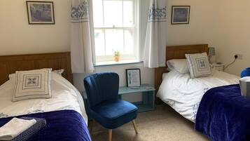 Una habitación de hotel con dos camas, una silla azul, una mesita y una ventana con cortinas.
