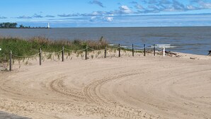 Una playa arenosa con una barrera de cuerda, un faro a lo lejos y un cielo despejado.