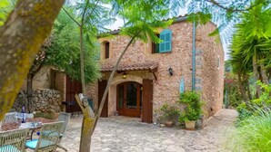 Un edificio de piedra con techo de tejas, puerta de madera y un pequeño patio con mesa y sillas.