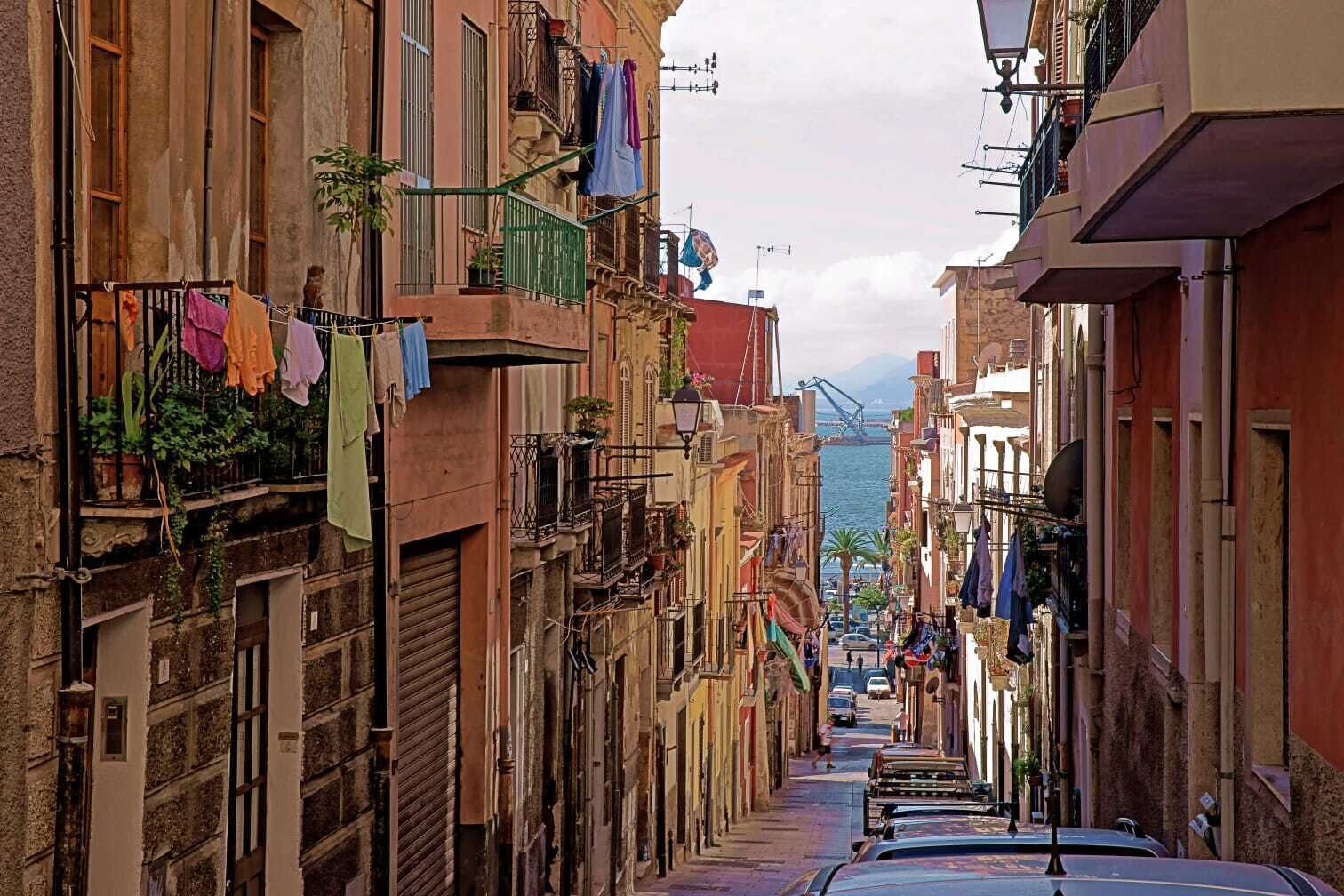 Une rue étroite bordée d’immeubles à plusieurs étages dotés de balcons, dont certains sont ornés de linge séchant.