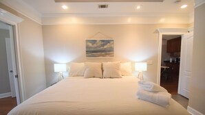 A neatly made bed with pillows and a folded towel, a painting of a landscape on the wall, and a doorway leading to a kitchen area. - Cozy 2-bedroom condo in charming Townsend with WiFi, AC (Townsend)