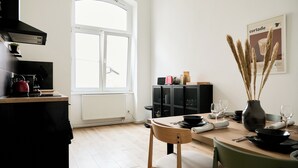 A modern kitchen with a large window, a dining table set for two, and a black cabinet with a red kettle on the counter. - Stylish Apartment in Berlin Mitte (Berlin)