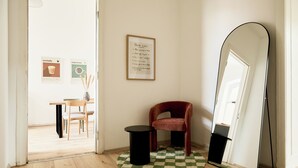 A room with a wooden floor, a round black table, a red chair, a framed sign on the wall, and a large mirror leaning against the wall. - Stylish Apartment in Berlin Mitte (Berlin)