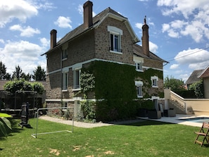 A stone house with a covered porch, a small pool, and a grassy yard.