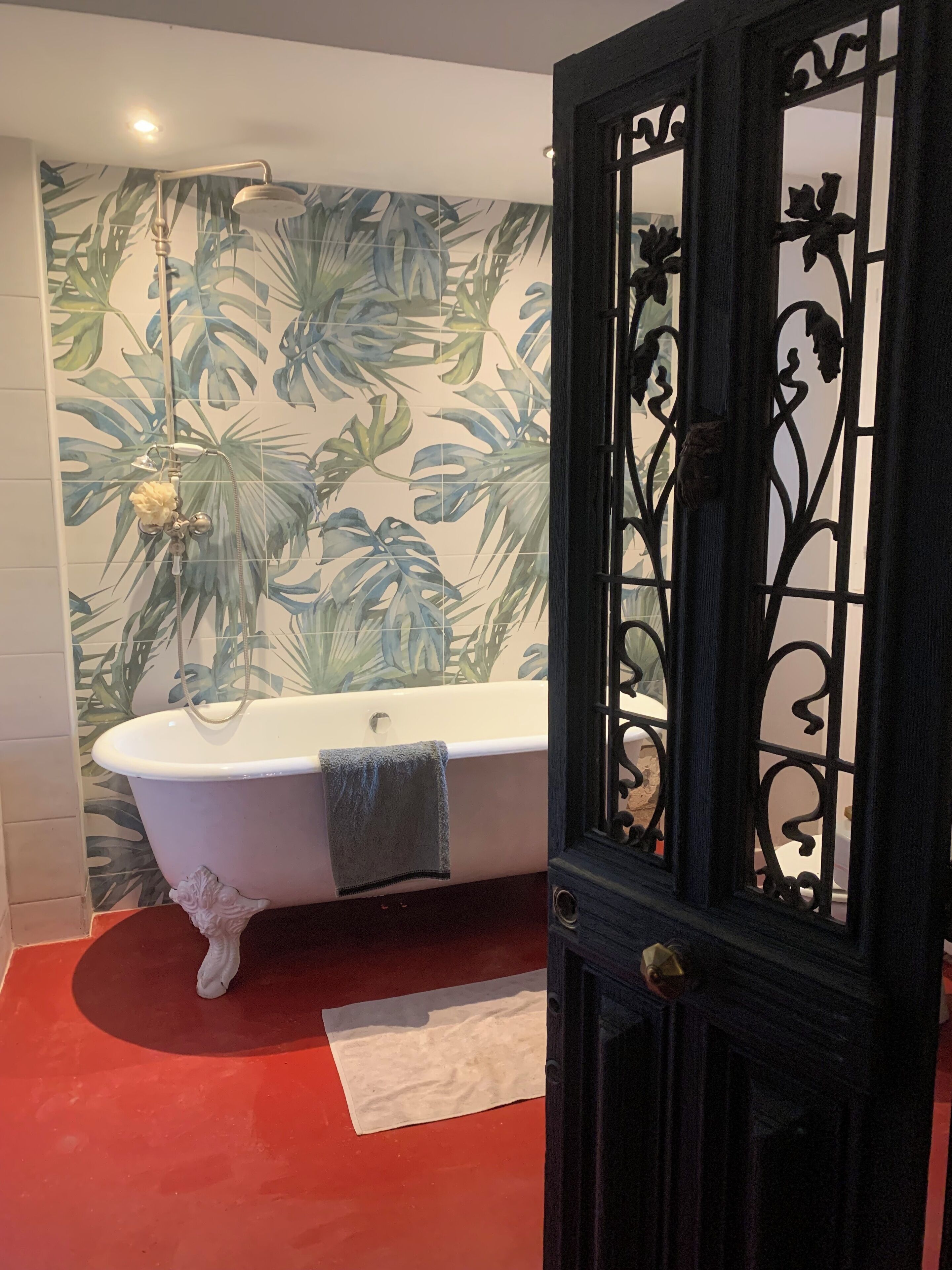 Un baño con una bañera independiente, cabezal de ducha y una puerta decorativa.