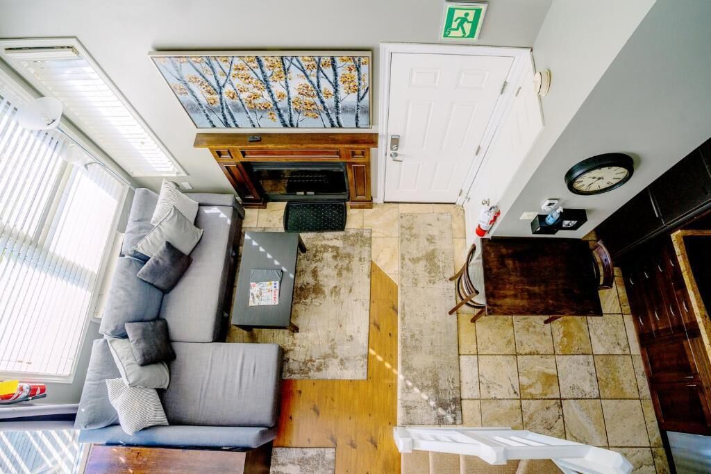 Een kamer met een bank, een kleine tafel, een open haard, een klok en een deur met een nooduitgangsbord.