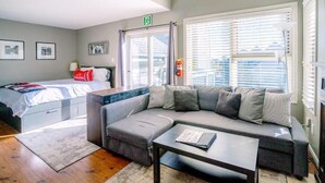 Een moderne hotelkamer met een bed, een bank, een bijzettafeltje en een raam met jaloezieën.