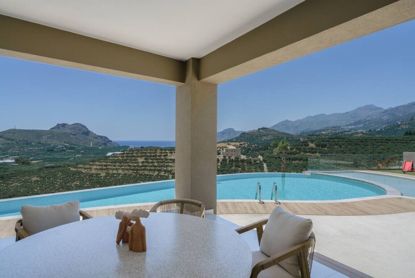 Une terrasse avec une table et des chaises donnant sur une piscine et un paysage montagneux.