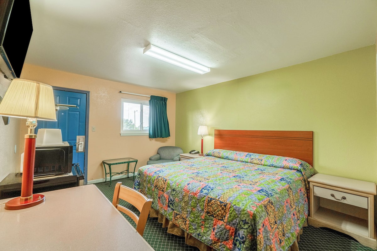 Une chambre d’hôtel avec un lit, un bureau, une chaise, une télévision et une lampe.