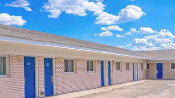 Un motel doté de nombreuses chambres, dont les portes sont numérotées, et un ciel dégagé parsemé de nuages.