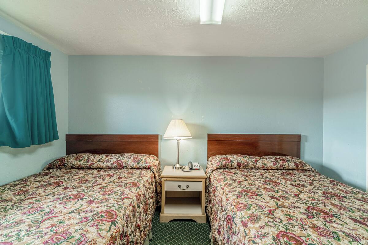 Une chambre d’hôtel avec deux lits, une table de chevet avec une lampe et un téléphone.
