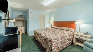 Habitación de hotel con cama, mesita de noche, lámpara y escritorio con ordenador.
