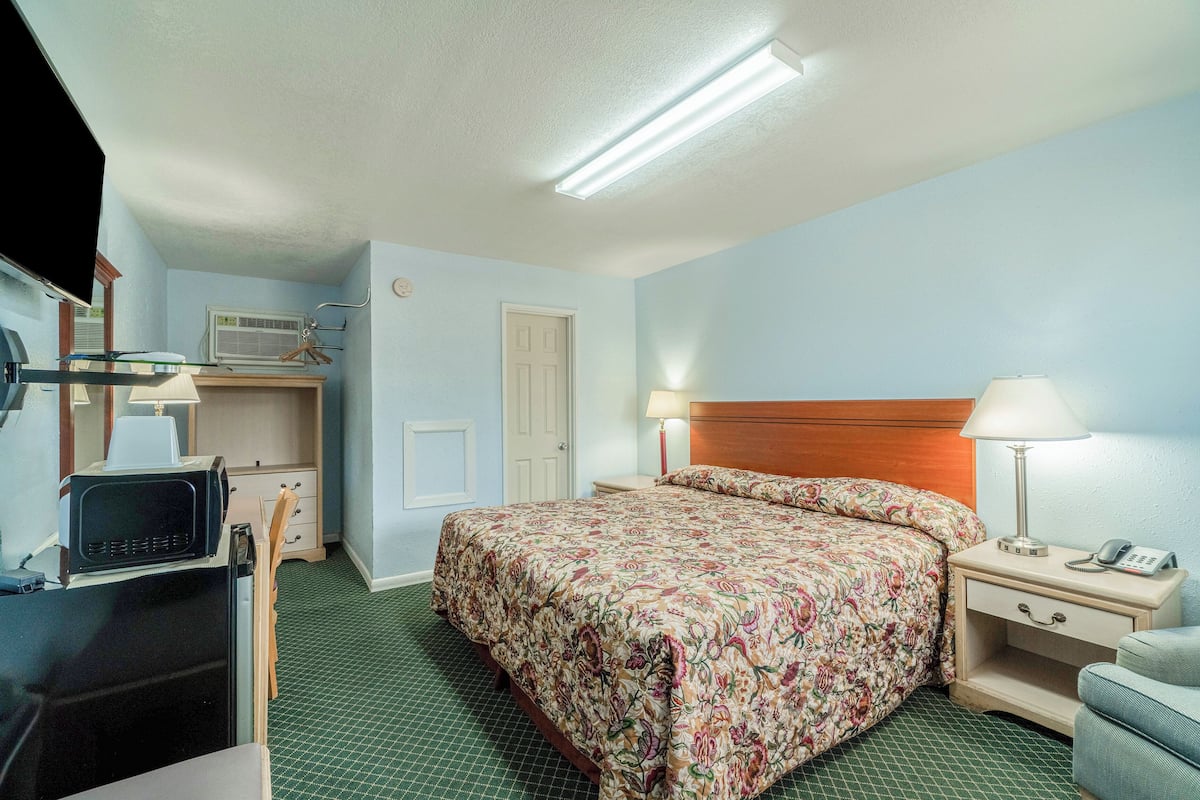 Une chambre d’hôtel équipée d’un lit, d’une table de chevet, d’une lampe et d’un bureau avec un ordinateur.