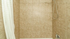 Un baño con azulejos color beige, un cabezal de ducha y una bañera.