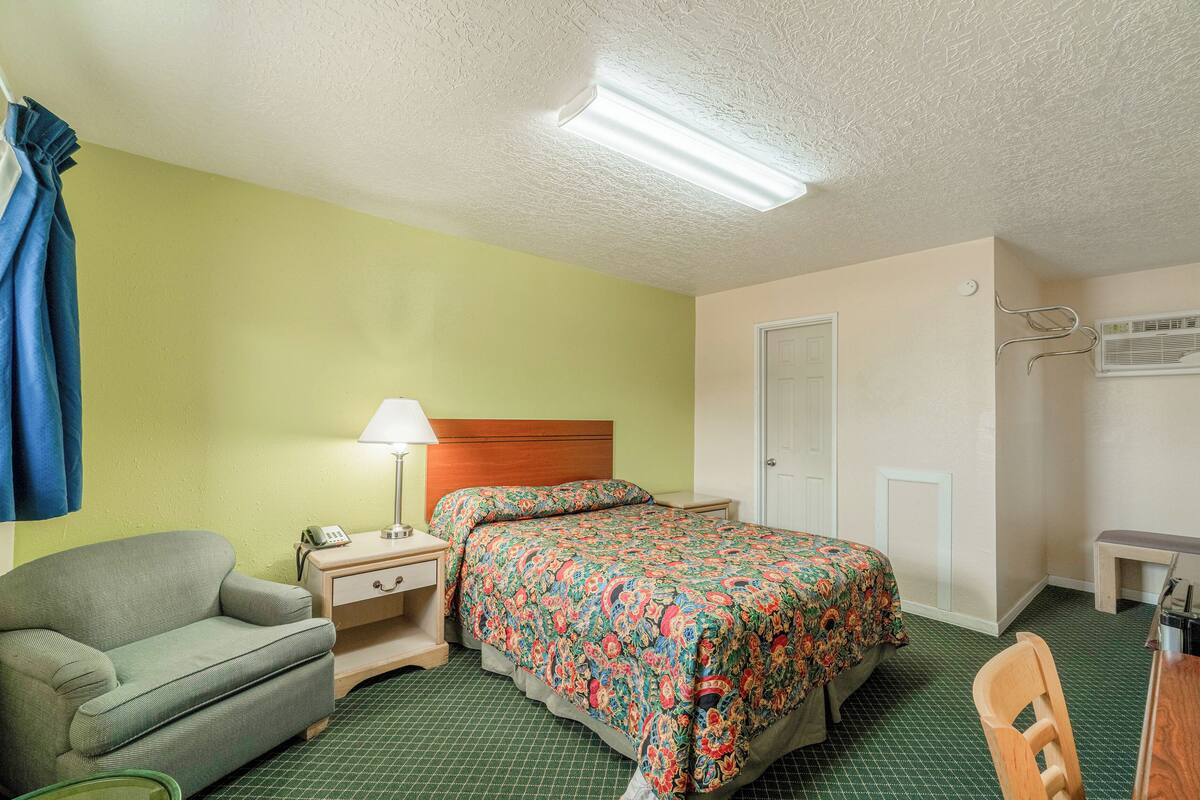 Une chambre d’hôtel avec un lit, une chaise, un bureau, une lampe et un téléphone.