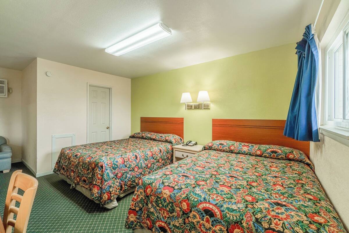 Une chambre d’hôtel avec deux lits, une table de chevet, une chaise et une fenêtre avec des rideaux.