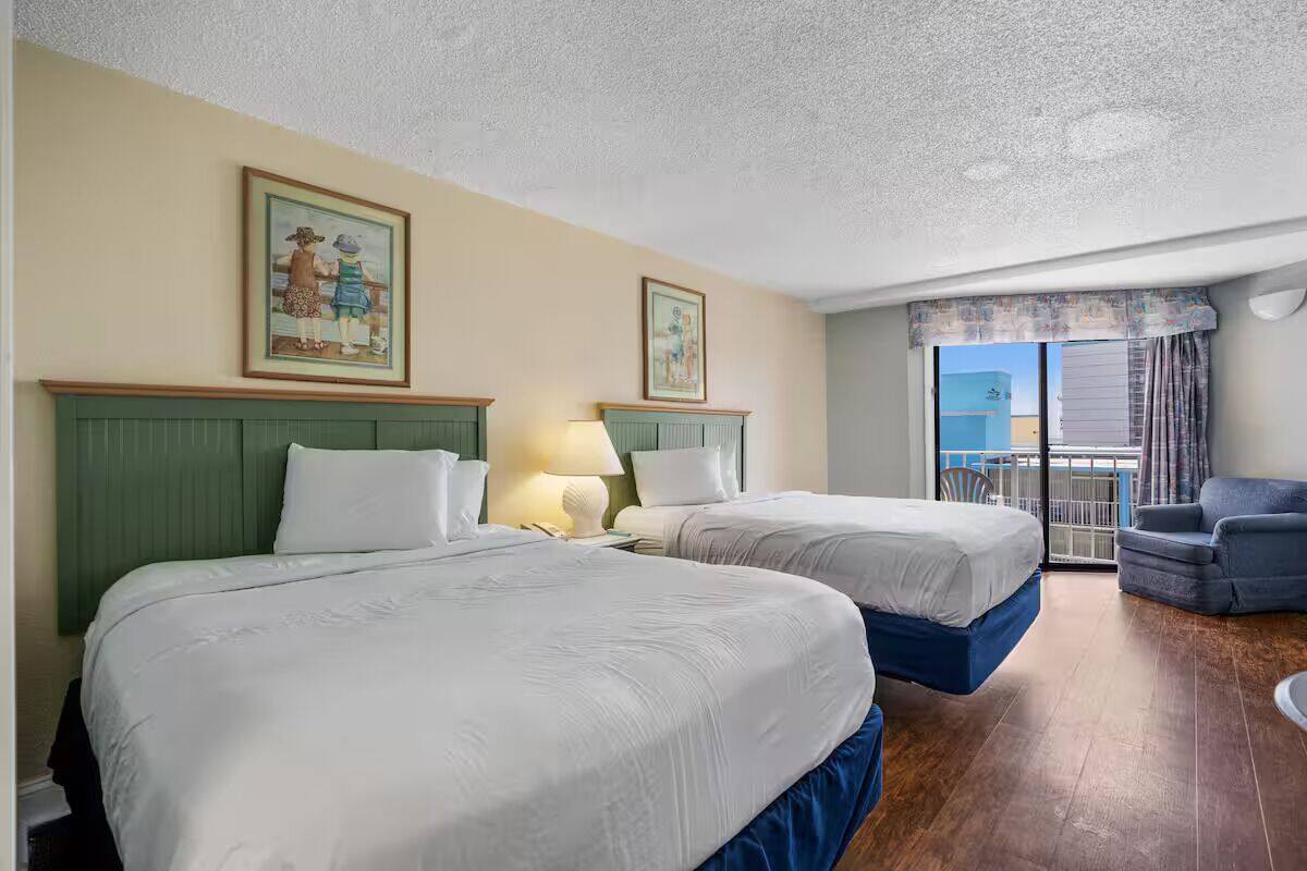 Habitación de hotel con dos camas, un balcón y vistas, además de una silla.