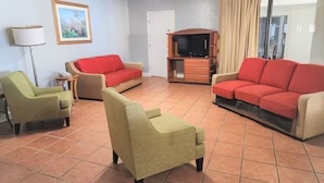 A living room with a red sofa, a green armchair, a beige armchair, a small table, and a television on a wooden stand. - Hotel O Sunset Waves Myrtle Beach, Sc (Myrtle Beach)