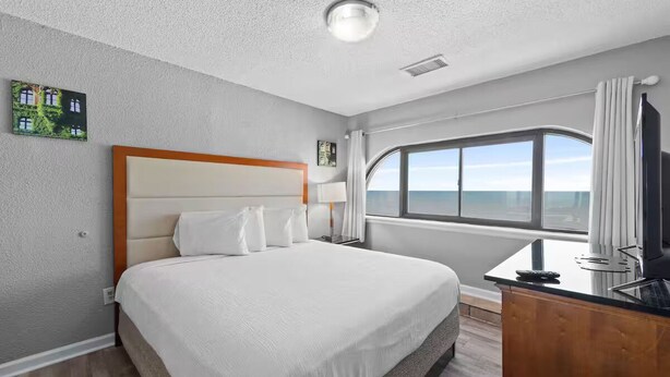 A hotel room with a large bed, a desk with a chair, a window with a view, and a ceiling light. - Hotel O Sunset Waves Myrtle Beach, Sc (Myrtle Beach)