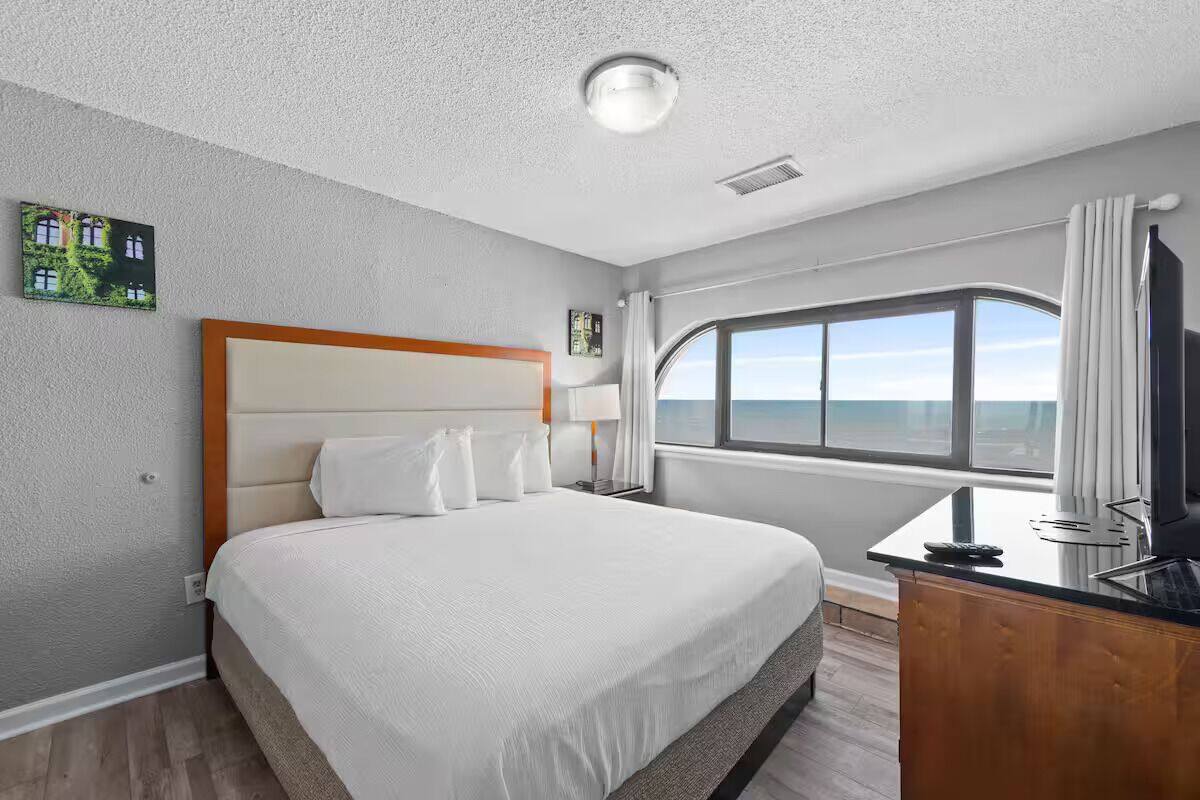 Habitación de hotel con una cama grande, un escritorio con silla, una ventana con vistas y una lámpara en el techo.