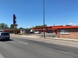 Um motel com fachada vermelha, estacionamento e céu azul.