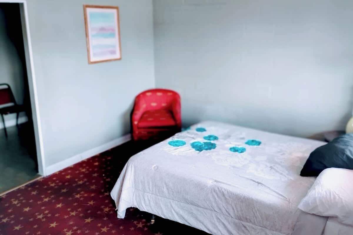 Una habitación con una cama, una silla roja y un cuadro en la pared.