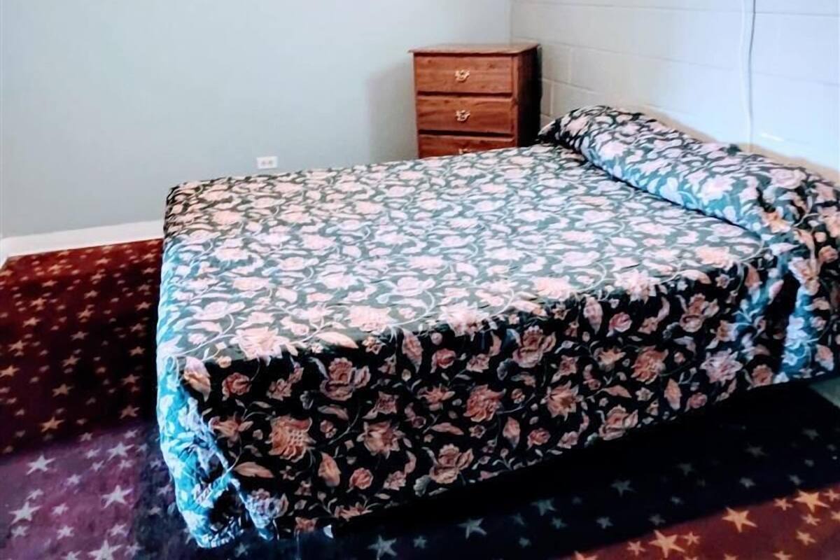 Un dormitorio con colcha estampada, mesita de noche de madera y alfombra roja.