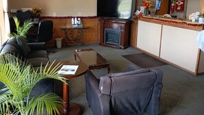 A living room with a sofa, armchair, coffee table, fireplace, TV, and a reception desk with a clock. - Hotel O Englewood-South Denver CO (Englewood)