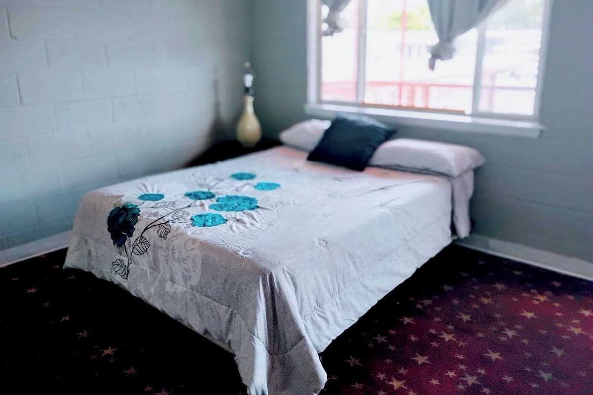 Un dormitorio con cama, ventana con cortinas y pared de ladrillo.