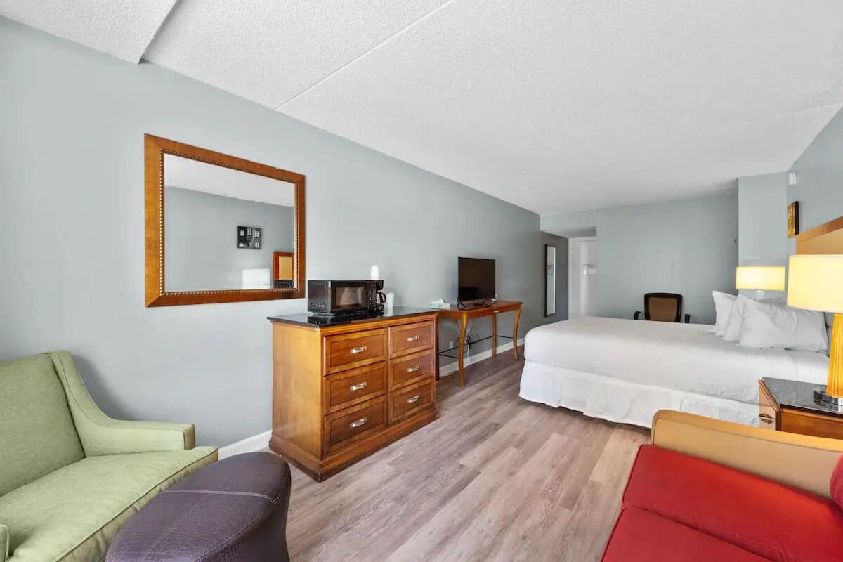 A hotel room with a bed, a desk with a computer, a dresser, and a couch.