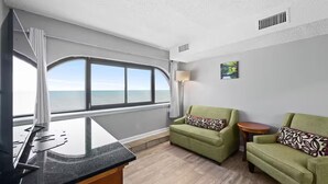A room with a large window, a desk with a computer, two green sofas, and a small table. - Capital O Sunset Waves Hotel Myrtle Beach Oceanfront (Myrtle Beach)
