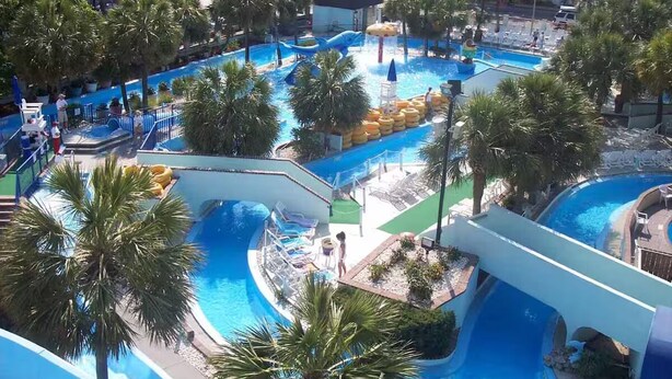 A large outdoor swimming pool area with multiple water slides and palm trees. - Capital O Sunset Waves Hotel Myrtle Beach Oceanfront (Myrtle Beach)