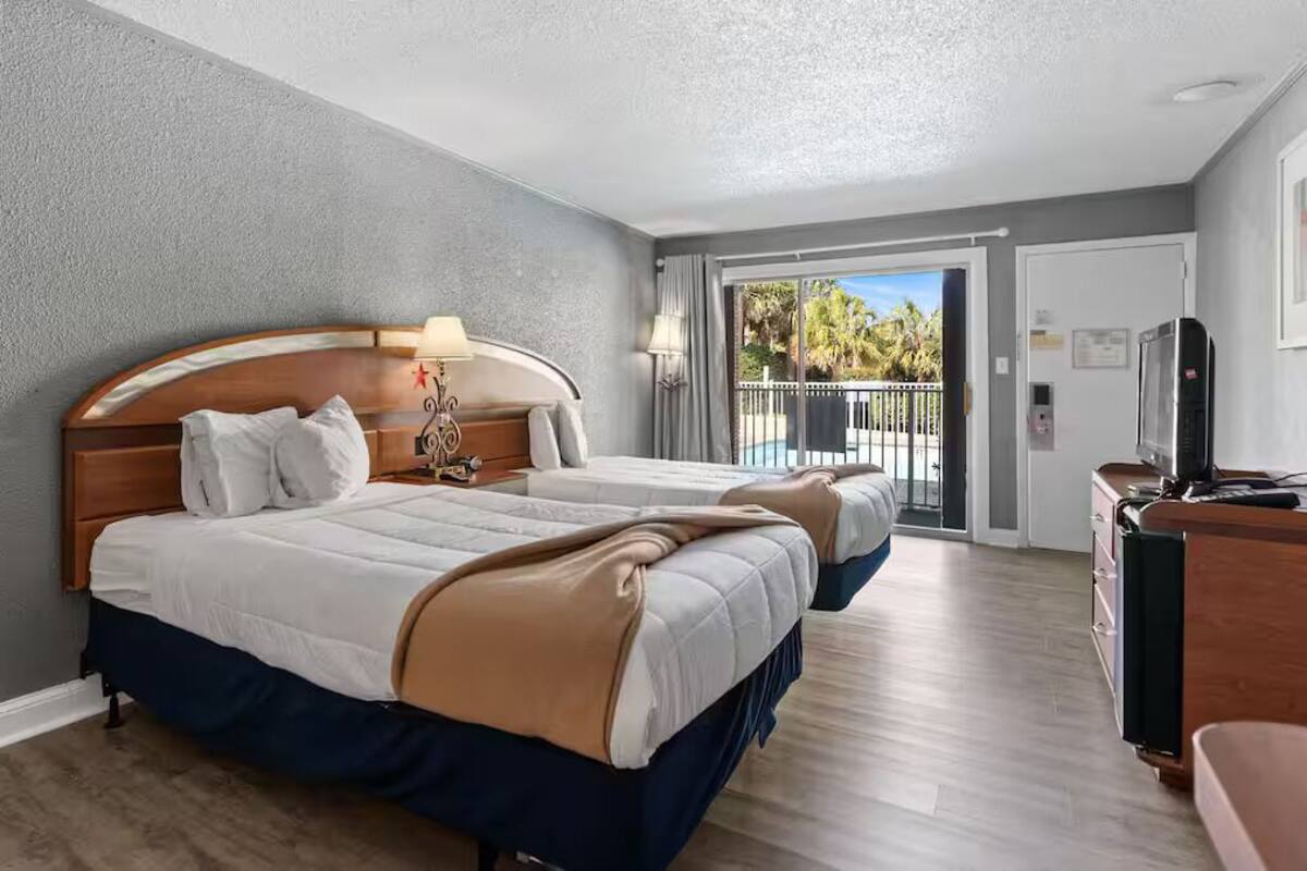 A hotel room with two beds, a balcony with a view, a desk with a computer, and a TV.
