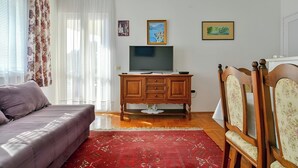 A living room with a sofa, a TV on a wooden cabinet, and two framed pictures on the wall. - Apartment RuzicaCharming 1-bedroom apartment with Sveti Stefan (sveti stefan)