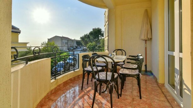A balcony with a table and chairs, a hanging lantern, and a view of the street and buildings. - Apartment RuzicaCharming 1-bedroom apartment with Sveti Stefan (sveti stefan)