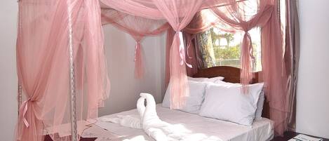 A bedroom with a four-poster bed, a wooden nightstand, and a window with curtains.
