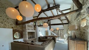 Un intérieur rustique avec des poutres apparentes, un mur en pierre, un grand canapé et des luminaires suspendus.