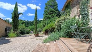 A gravel pathway leading to a wooden deck with metal chairs. - Charming historic barn with pool (Lembras)