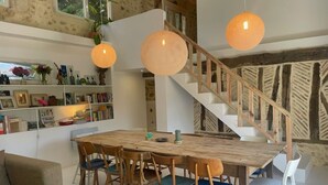 A modern living room with a wooden dining table, chairs, a sofa, and a staircase. - Charming historic barn with pool (Lembras)