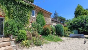 Une maison en pierre aux murs recouverts de lierre, avec une terrasse en bois et une cour en gravier.