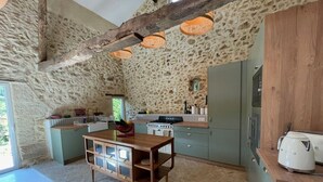 Une cuisine rustique aux murs en pierre, aux poutres apparentes et au sol décoré d’un motif en chevrons.