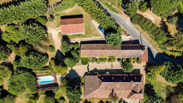 An aerial view of a residential area with multiple houses, a swimming pool, and a road. - Charming historic barn with pool (Lembras)