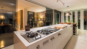 Una cocina moderna con una isla grande, electrodomésticos integrados y un panel de vidrio que la separa del comedor.