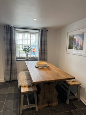 A dining area with a wooden table, bench seating, a potted plant, and a window with curtains.