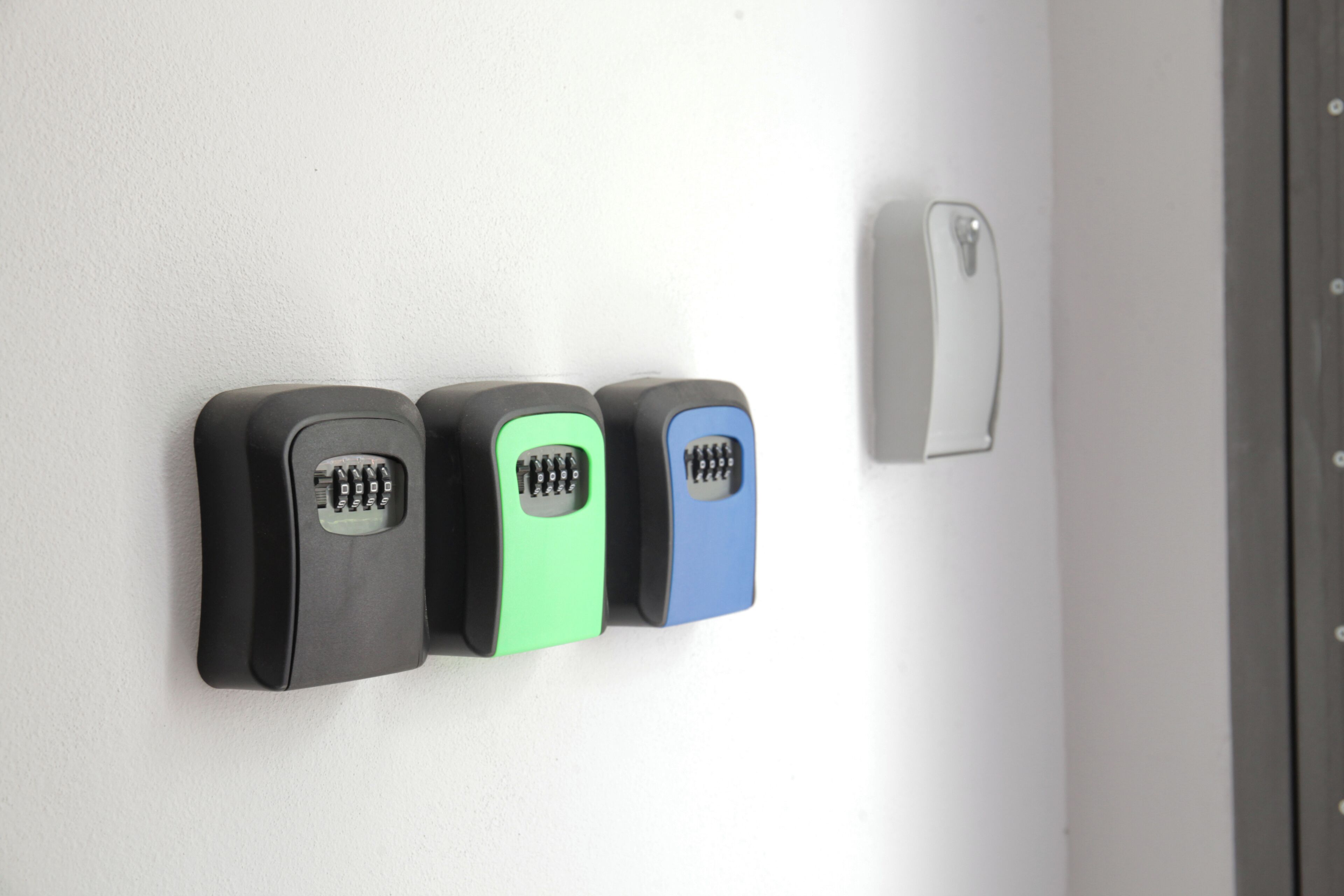 A wall-mounted security keypad with three buttons in black, green, and blue.